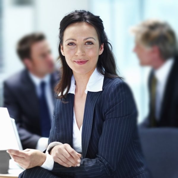 Portrait of business woman smiling with executives discussing in background